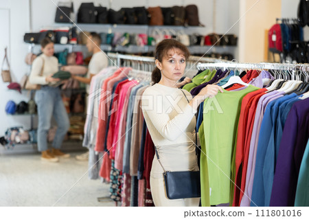 Woman buyer in store has removed hanger with blouse from window and is considering product. 111801016