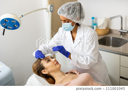 Female cosmetologist marking skin of young woman with white pencil Female cosmetologist marking skin of young woman with white pencil 111801045