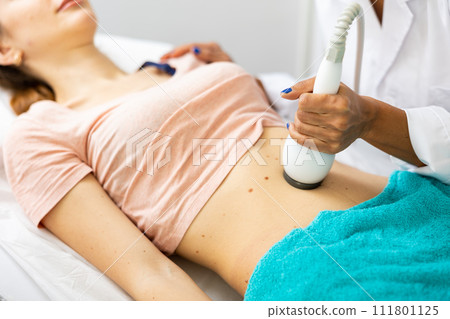 Beautician doing ultrasound lifting procedure in woman's abdominal region Beautician doing ultrasound lifting procedure in woman's abdominal region 111801125