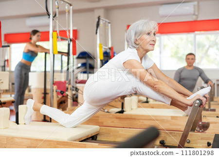 Elderly woman doing stretching on pilates machine Elderly woman doing stretching on pilates machine 111801298