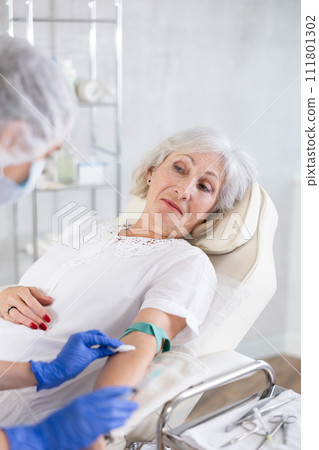 Young doctor drawing blood from elderly patient. Young doctor drawing blood from elderly patient. 111801302