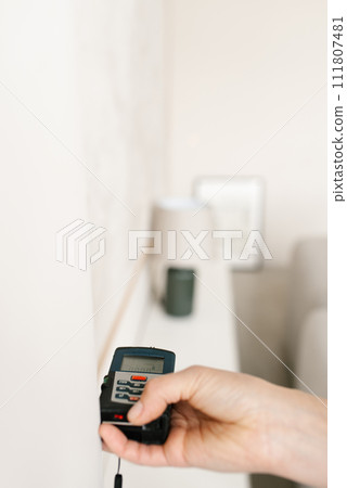 Laser rangefinder in the hands of a woman near a wall. Engineer holding laser rangefinder close up with copy space 111807481