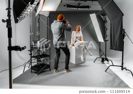 Man photographing woman sitting on cube in photo studio Man photographing woman sitting on cube in photo studio 111809514
