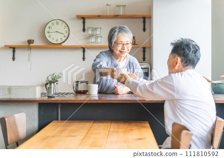 Senior woman/wife/wife passing coffee from the kitchen Senior man/husband receiving coffee 111810592