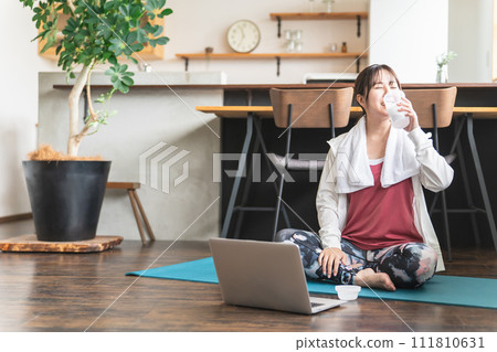 Young Asian woman drinking protein/BCAA after training in her living room 111810631