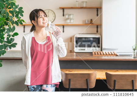 Asian woman hydrating with bottled mineral water after home training Asian woman hydrating with bottled mineral water after home training 111810645