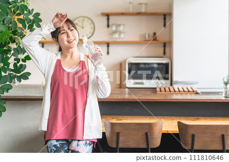 Asian woman hydrating with bottled mineral water after home training Asian woman hydrating with bottled mineral water after home training 111810646