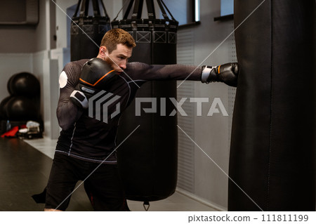 Boxer practicing on heavy bag while training in modern gym 111811199
