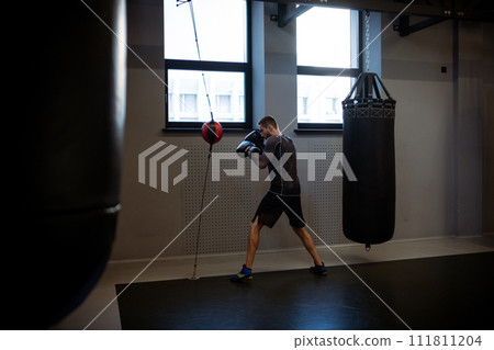 Man in boxing gloves training with floor to ceiling bag 111811204