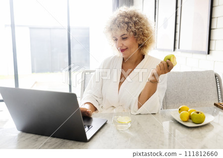 Woman Healthy Morning. Female in White Robe Enjoying Morning Breakfast with Laptop. Smiling Woman Healthy Morning. Female in White Robe Enjoying Morning Breakfast with Laptop. Smiling 111812660
