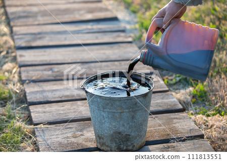 Pour used motor oil from a can into a metal bucket. Pour used motor oil from a can into a metal bucket. 111813551