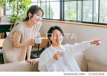 Couple watching TV while drinking coffee on the sofa in the living room at home Couple watching TV while drinking coffee on the sofa in the living room at home 111813828