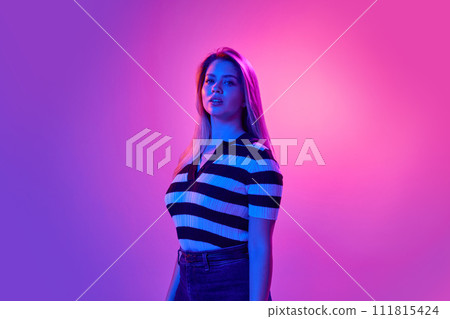 Gel portrait of beautiful young woman with blonde hair, wearing stripped shirt, posing against pink studio background in neon light Gel portrait of beautiful young woman with blonde hair, wearing stripped shirt, posing against pink studio background in neon light 111815424