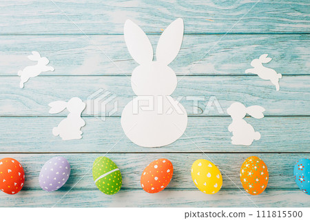 Easter Day Concept. Top view holiday banner background web design white colorful easter eggs and paper bunny rabbit on blue wood background with copy space, celebration greeting, overhead, template Easter Day Concept. Top view holiday banner background web design white colorful easter eggs and paper bunny rabbit on blue wood background with copy space, celebration greeting, overhead, template 111815500