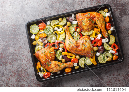 Delicious Mediterranean baked chicken legs with vegetables and feta cheese close-up on a baking sheet on the table. Horizontal top view Delicious Mediterranean baked chicken legs with vegetables and feta cheese close-up on a baking sheet on the table. Horizontal top view 111815604
