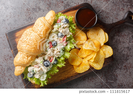 Chicken salad on a flaky butter croissant with potato chips on a wooden board. Horizontal top view Chicken salad on a flaky butter croissant with potato chips on a wooden board. Horizontal top view 111815617