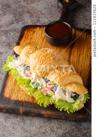 Croissant sandwich with salad made from chicken, grapes, onions, celery, dressed with mayonnaise close-up on a wooden board. Vertical Croissant sandwich with salad made from chicken, grapes, onions, celery, dressed with mayonnaise close-up on a wooden board. Vertical 111815628