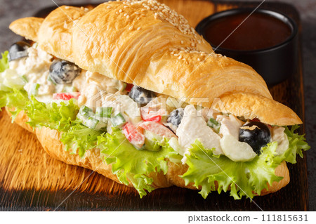 Closeup of a chicken salad and lettuce sandwich on a croissant roll on a wooden board. Horizontal Closeup of a chicken salad and lettuce sandwich on a croissant roll on a wooden board. Horizontal 111815631