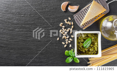 Homemade pesto sauce in small white square jar and ingredients for pasta on black slate background Homemade pesto sauce in small white square jar and ingredients for pasta on black slate background 111815905