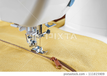Modern sewing machine with special presser foot on yellow velours fabric close up Modern sewing machine with special presser foot on yellow velours fabric close up 111815909