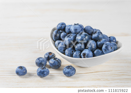 Fresh blueberries in a small round white bowl on white wooden background Fresh blueberries in a small round white bowl on white wooden background 111815922