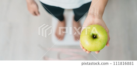 woman on weight scale and hand hold green Apple, choose fruit is Healthy food. Dieting control, Weight loss, Obesity, eating lifestyle and nutrition concepts woman on weight scale and hand hold green Apple, choose fruit is Healthy food. Dieting control, Weight loss, Obesity, eating lifestyle and nutrition concepts 111816881