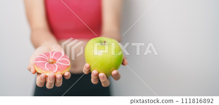 woman hand hold green Apple and donut, female fitness choose between fruit is Healthy and sweet is Unhealthy junk food. Dieting control, Weight loss, Obesity, eating lifestyle and nutrition concept woman hand hold green Apple and donut, female fitness choose between fruit is Healthy and sweet is Unhealthy junk food. Dieting control, Weight loss, Obesity, eating lifestyle and nutrition concept 111816892