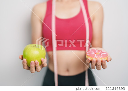 woman hand hold green Apple and donut, female fitness choose between fruit is Healthy and sweet is Unhealthy junk food. Dieting control, Weight loss, Obesity, eating lifestyle and nutrition concept 111816893