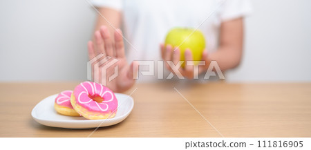 woman hand hold green Apple and reject donut, female fitness choose between fruit is Healthy and sweet is Unhealthy junk food. Dieting control, Weight loss, Obesity, eating lifestyle and nutrition woman hand hold green Apple and reject donut, female fitness choose between fruit is Healthy and sweet is Unhealthy junk food. Dieting control, Weight loss, Obesity, eating lifestyle and nutrition 111816905