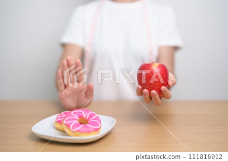 woman hand hold red Apple and reject donut, female fitness choose between fruit is Healthy and sweet is Unhealthy junk food. Dieting control, Weight loss, Obesity, eating lifestyle and nutrition woman hand hold red Apple and reject donut, female fitness choose between fruit is Healthy and sweet is Unhealthy junk food. Dieting control, Weight loss, Obesity, eating lifestyle and nutrition 111816912