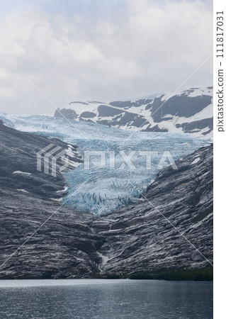 Vertical frame showcases towering Svartisen Glacier descending into the waters of a Norwegian lake 111817031