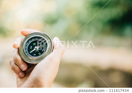 In the forest a hiker uses a compass to conquer confusion and find direction. The compass in the traveler hand represents topography and discovery amidst nature beauty. In the forest a hiker uses a compass to conquer confusion and find direction. The compass in the traveler hand represents topography and discovery amidst nature beauty. 111817434