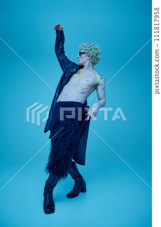 Full length portrait of artistic young man with naked torso in long black leather jacket dancing against blue studio background. Full length portrait of artistic young man with naked torso in long black leather jacket dancing against blue studio background. 111817958