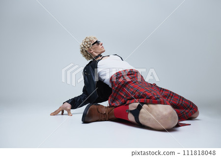Performative street style portrait of young man showcasing eclectic mix of traditional and modern fashion against grey studio background. 111818048