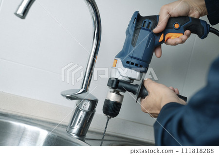 man drilling a hole in a metal sink 111818288