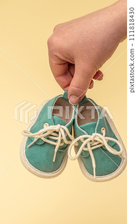 A pair of small child's shoes in a hand on a yellow background. Newborn concept 111818430