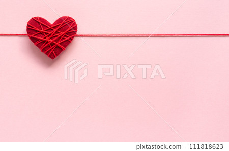 A red heart on a pink background A heart wrapped around with thread 111818623