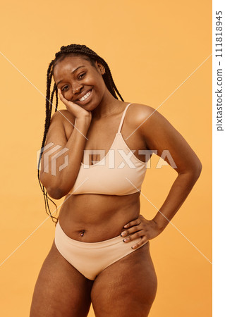 Studio portrait of modern young African American woman with braided hair wearing comfortable lingerie posing for camera, warm apricot background Studio portrait of modern young African American woman with braided hair wearing comfortable lingerie posing for camera, warm apricot background 111818945