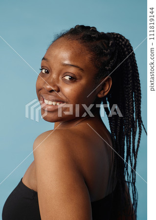 Vertical medium closeup of self-confident African American girl with braided hair posing for camera in studio, baby blue background 111819144