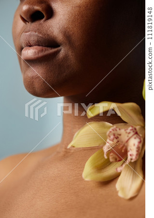 Vertical closeup crop studio shot of young Black woman with fresh orchid flower on collarbone Vertical closeup crop studio shot of young Black woman with fresh orchid flower on collarbone 111819148