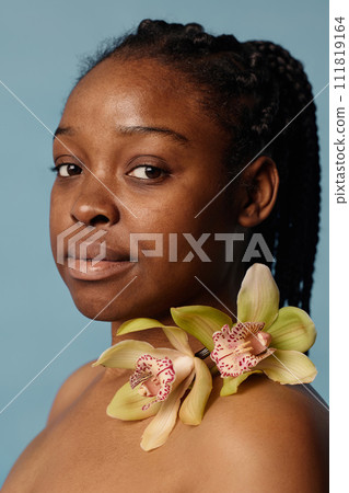Vertical closeup portrait of beautiful young Black woman with no makeup posing for camera with fresh orchid flowers Vertical closeup portrait of beautiful young Black woman with no makeup posing for camera with fresh orchid flowers 111819164