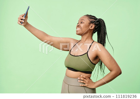 Medium portrait of modern young Black woman with braided hair wearing activewear standing in studio posing for selfie photos Medium portrait of modern young Black woman with braided hair wearing activewear standing in studio posing for selfie photos 111819236