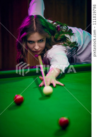 Concentrated young woman leaning on billiards table, playing snooker game. Lifestyle magazine about leisure activities Concentrated young woman leaning on billiards table, playing snooker game. Lifestyle magazine about leisure activities 111819798
