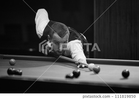 Focused young man leaning on billiards table, aiming cue on balls, playing snooker game. Online course banner for mastering billiards skills. 111819850