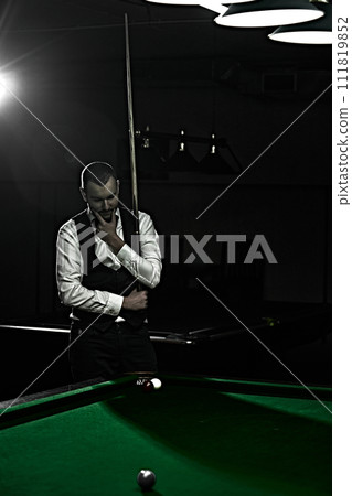 Handsome young man with cue in billiard hall, dressed in waistcoat and white shirt. Promotion of billiards-themed events. Colorful focus on table Handsome young man with cue in billiard hall, dressed in waistcoat and white shirt. Promotion of billiards-themed events. Colorful focus on table 111819852
