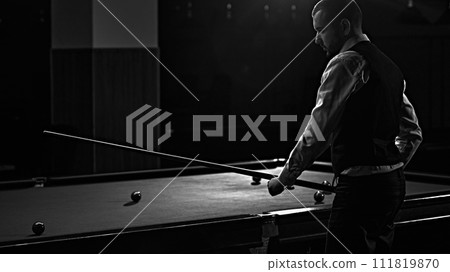 Man in waistcoat playing snooker game, billiards, monochrome image capturing intense focus. Luxury space for billiards game Man in waistcoat playing snooker game, billiards, monochrome image capturing intense focus. Luxury space for billiards game 111819870