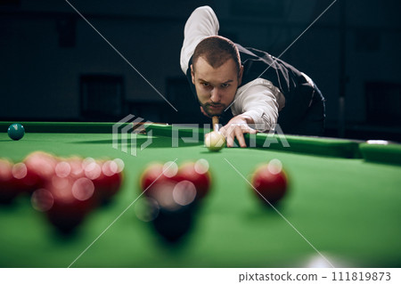 Concentrated young man leaning on billiards table, playing snooker game. Lifestyle magazine spread highlighting leisure activities Concentrated young man leaning on billiards table, playing snooker game. Lifestyle magazine spread highlighting leisure activities 111819873