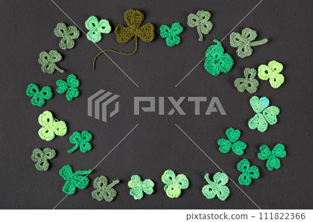 St Patrick's Day concept. Composition made of knitted green shamrocks on a black background. Holiday sign and knitted clover leaf. Copy space, flat lay, place for text 111822366
