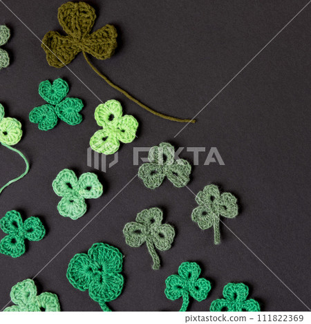 St Patrick's Day concept. Composition made of knitted green shamrocks on a black background. Holiday sign and knitted clover leaf. 111822369