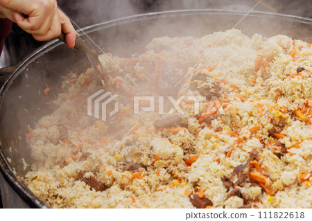 Cooking tasty traditional Uzbek pilaf in cauldron at street food festival Cooking tasty traditional Uzbek pilaf in cauldron at street food festival 111822618